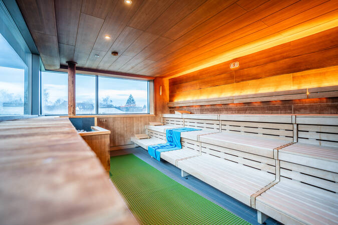 Eine moderne Sauna mit Holzinterieur, mehreren Sitzreihen und einem großen Fenster, das Tageslicht hereinlässt.