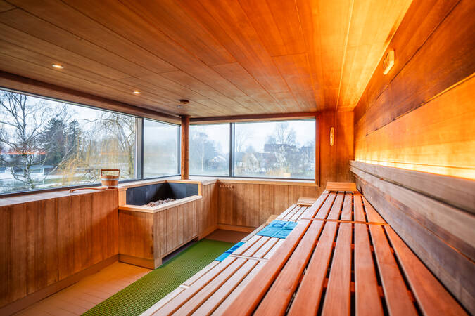 Eine moderne Sauna mit Holzinterieur, mehreren Sitzreihen und einem großen Fenster, das Tageslicht hereinlässt.