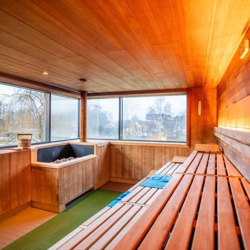 Eine moderne Sauna mit Holzinterieur, mehreren Sitzreihen und einem großen Fenster, das Tageslicht hereinlässt.