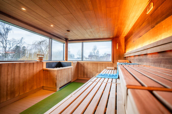 Eine moderne Sauna mit Holzinterieur, mehreren Sitzreihen und einem großen Fenster, das Tageslicht hereinlässt.