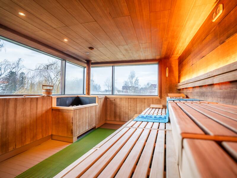Eine moderne Sauna mit Holzinterieur, mehreren Sitzreihen und einem großen Fenster, das Tageslicht hereinlässt.