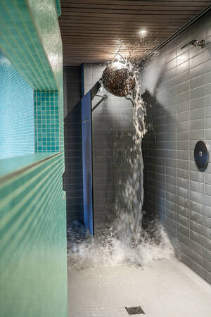Schwallbrause als Eimer der gerade Wasser ausschüttet im grün und grau gekachelten Duschbereich einer Sauna