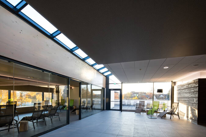 Der Raum zeigt eine entspannende Lounge mit mehreren Liegestühlen, großen Glasfenstern und Blick auf einen Außenbereich.