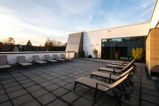 Eine geräumige Dachterrasse mit mehreren Liegestühlen, umgeben von modernen Gebäuden und Pflanzen, unter einem klaren Himmel.