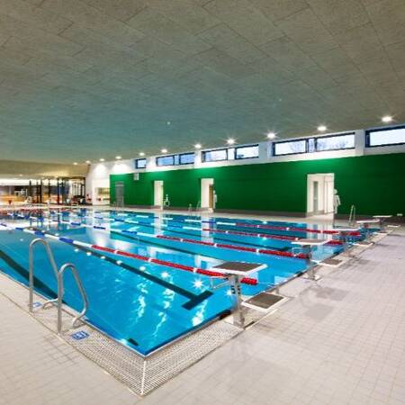 Ein großes Hallenbad mit mehreren Schwimmbahnen in einer modernen und gut beleuchteten Umgebung.