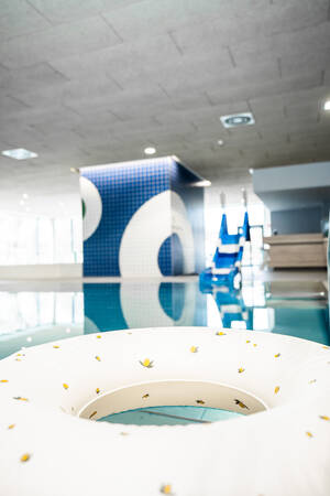 Ein Schwimmbad mit einem aufblasbaren Schwimmring im Vordergrund und einer blauen Kachelwand sowie einer Rutsche im Hintergrund.